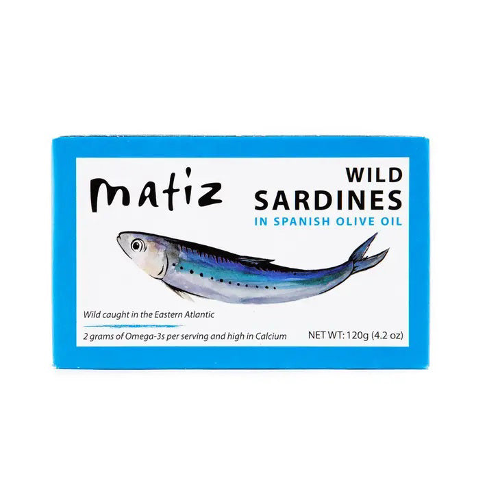 A blue rectangular box of Matiz España Wild Caught Smoked Sardines in organic olive oil, with a dash of sea salt. The illustration highlights the product's high Omega-3 and calcium content. Net weight: 120g (4.2 oz). These wild-caught sardines hail from the Eastern Atlantic for an authentic flavor experience.