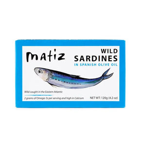 A blue rectangular box of Matiz España Wild Caught Smoked Sardines in organic olive oil, with a dash of sea salt. The illustration highlights the product's high Omega-3 and calcium content. Net weight: 120g (4.2 oz). These wild-caught sardines hail from the Eastern Atlantic for an authentic flavor experience.