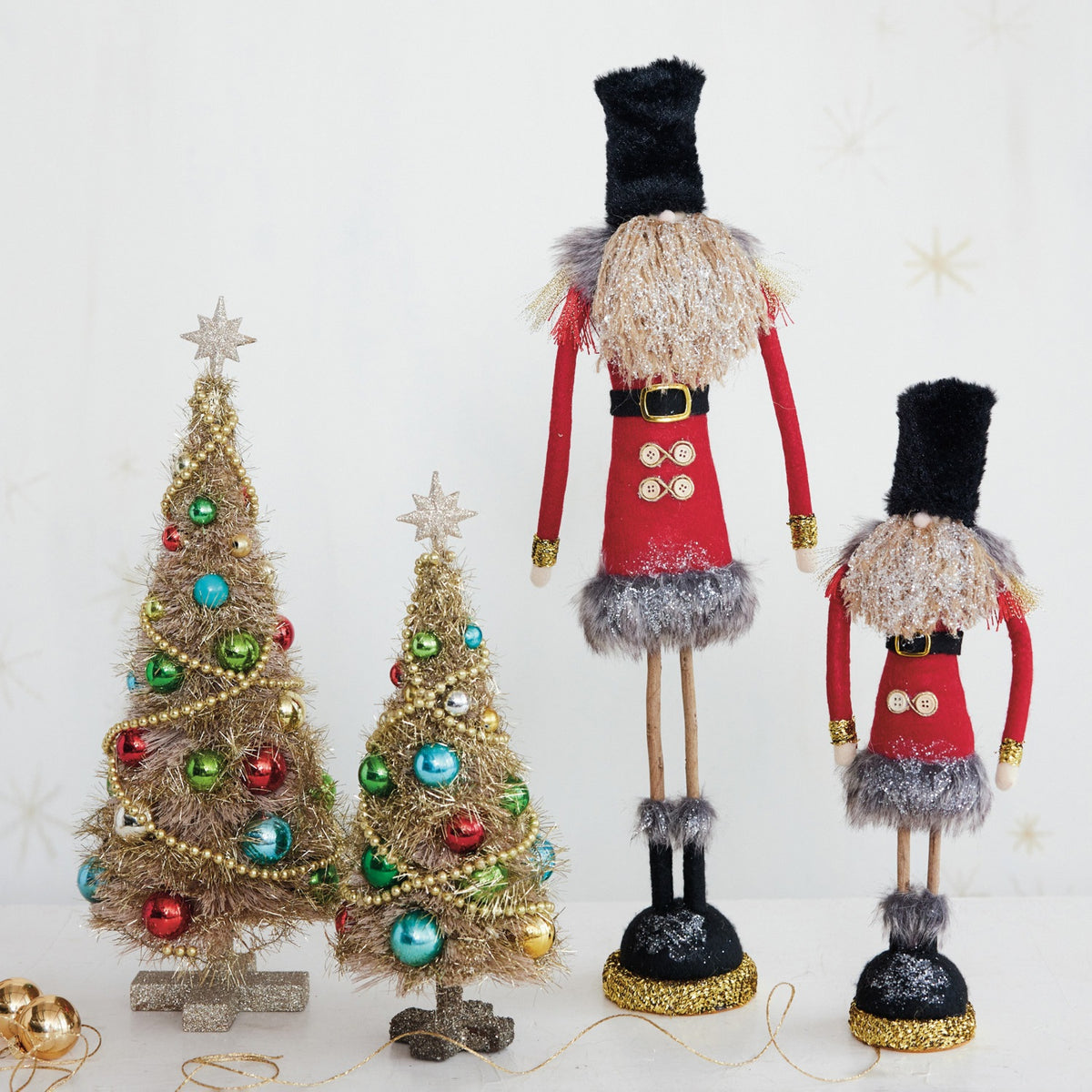 SOLDIER WITH GLITTER AND TWIG LEGS whimsical fabric figurine with a tall black hat, red coat, two buttons, and twig legs standing on a glittery gold and black base.