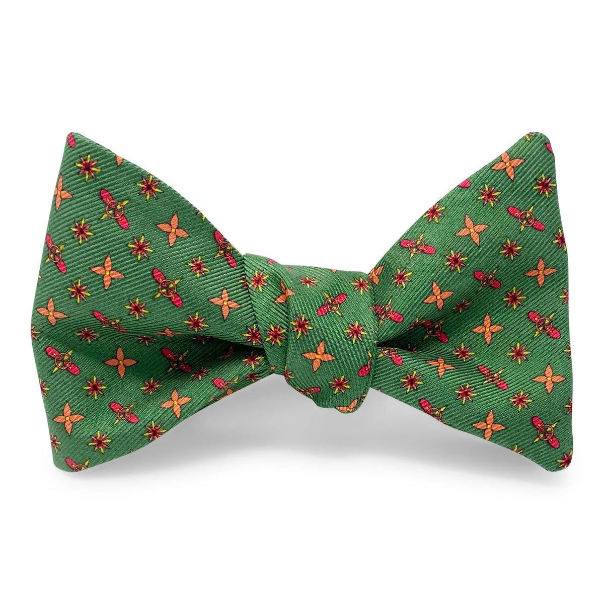 The BIRD DOG BAY PETER-BLAIR Foulard Silk Bow Tie in Green features a repeating red and yellow cross pattern, displayed flat against a white background. This adjustable neck bow tie blends timeless style with modern versatility.