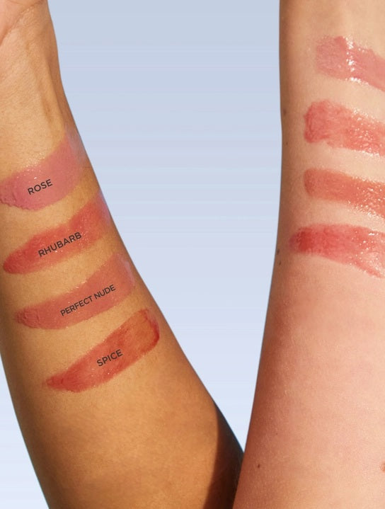 Two forearms with four swatches of LANOLIPS - TINTED LANOLIN LIP BALM IN ROSE shades—Rose, Rhubarb, Perfect Nude, and Spice—display color differences on different skin tones against a light background. Each shade from LANOLIPS offers a look reminiscent of a sheer color lip tint or the subtle hydration delivered by this tinted lanolin lip balm.
