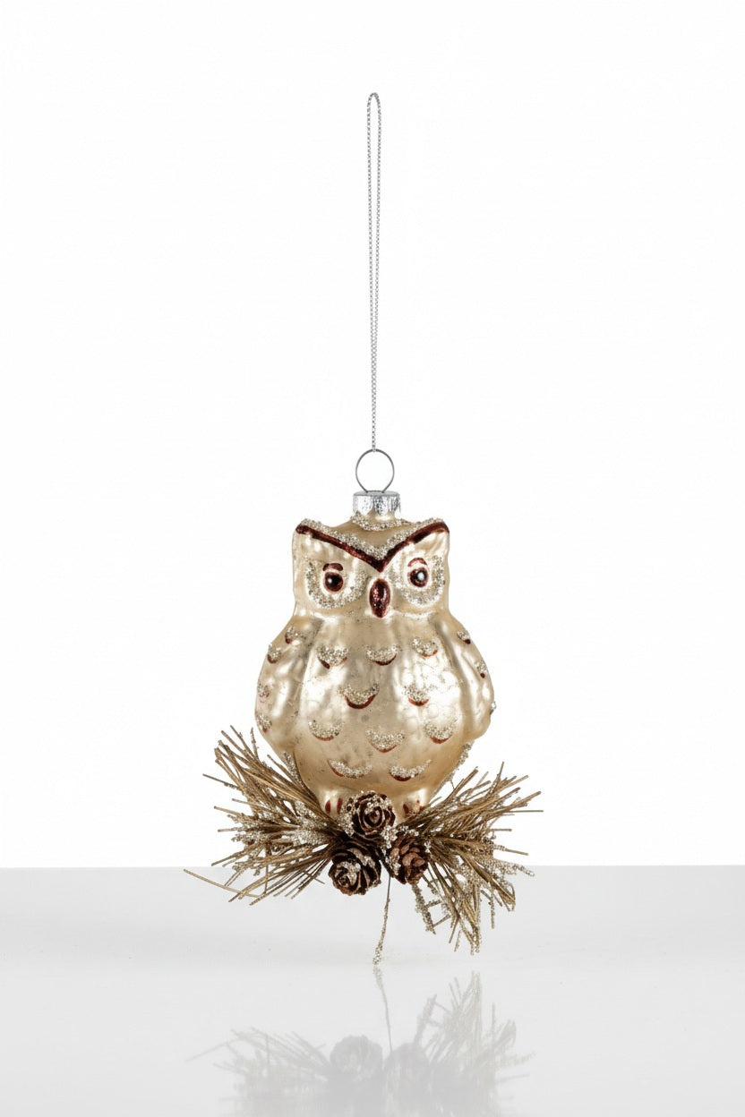 A GLASS OWL ORNAMENT WITH GLITTER perched on a cluster of pine needles and small glitter pinecones.