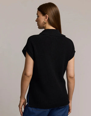 A woman with straight brown hair wears the HINSON WU - BROOKE SLEEVELESS SWEATER VEST in black with a gold-tone half-zip and blue jeans, standing facing forward against a plain light grey background.