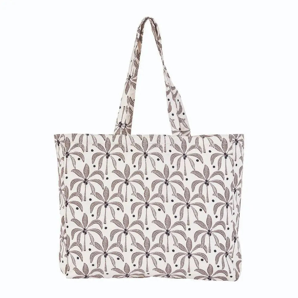 The ROCKFLOWERPAPER PALM SHOPPER TOTE BAG is a spacious cotton canvas bag with two handles, featuring a stylish brown palm tree print on a white background.