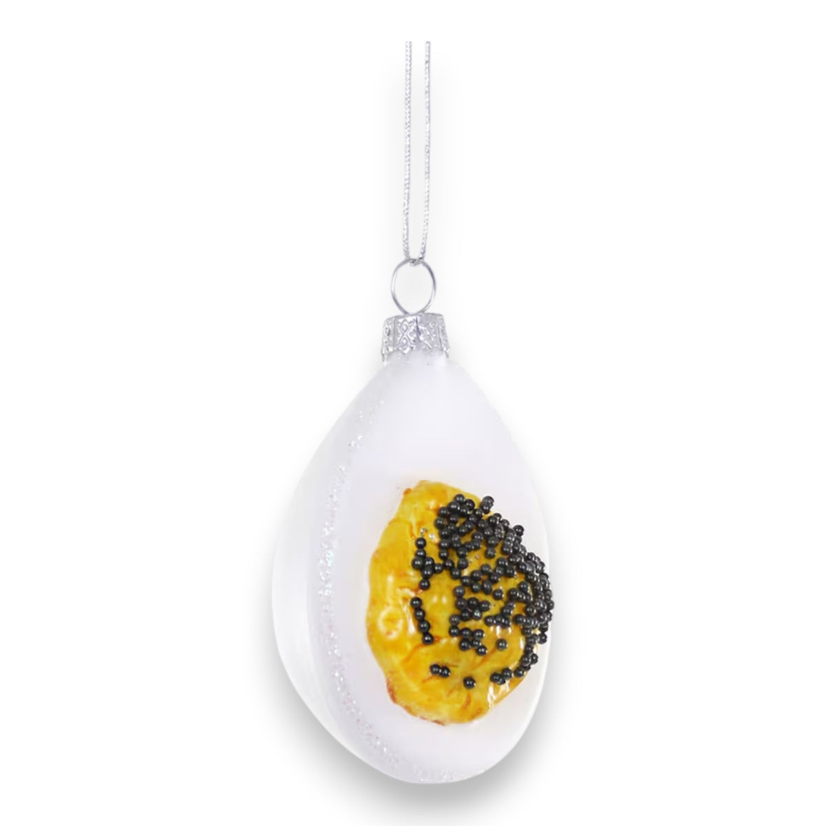 The CODY FOSTER DEVILED EGG WITH CAVIAR ORNAMENT features a halved egg with black bead &quot;caviar,&quot; hanging by a silver string—a whimsical addition for design lovers or collectors.