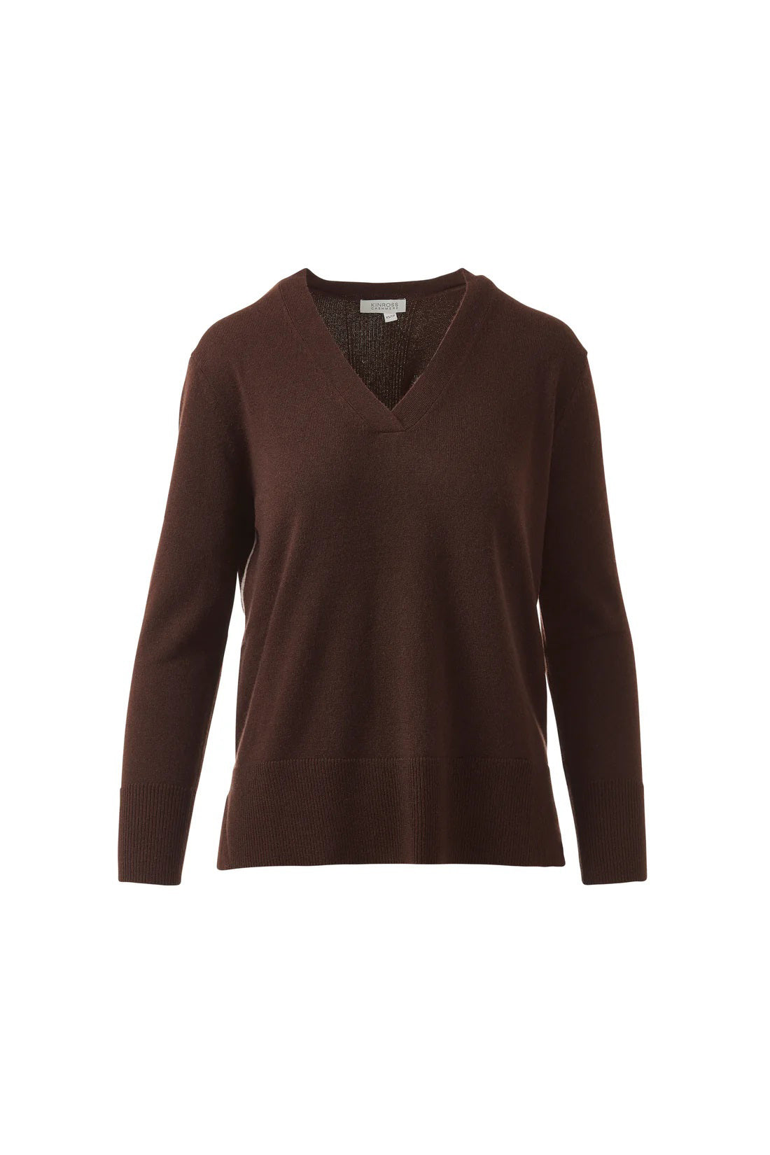 A woman with long brown hair models the KINROSS CASHMERE Hi Low Side Piped Easy Vee Neck Sweater by KINROSS, paired with blue jeans, standing against a plain white background and smiling slightly at the camera.