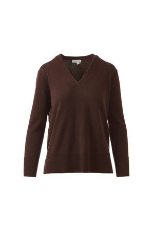 A woman with long brown hair models the KINROSS CASHMERE Hi Low Side Piped Easy Vee Neck Sweater by KINROSS, paired with blue jeans, standing against a plain white background and smiling slightly at the camera.