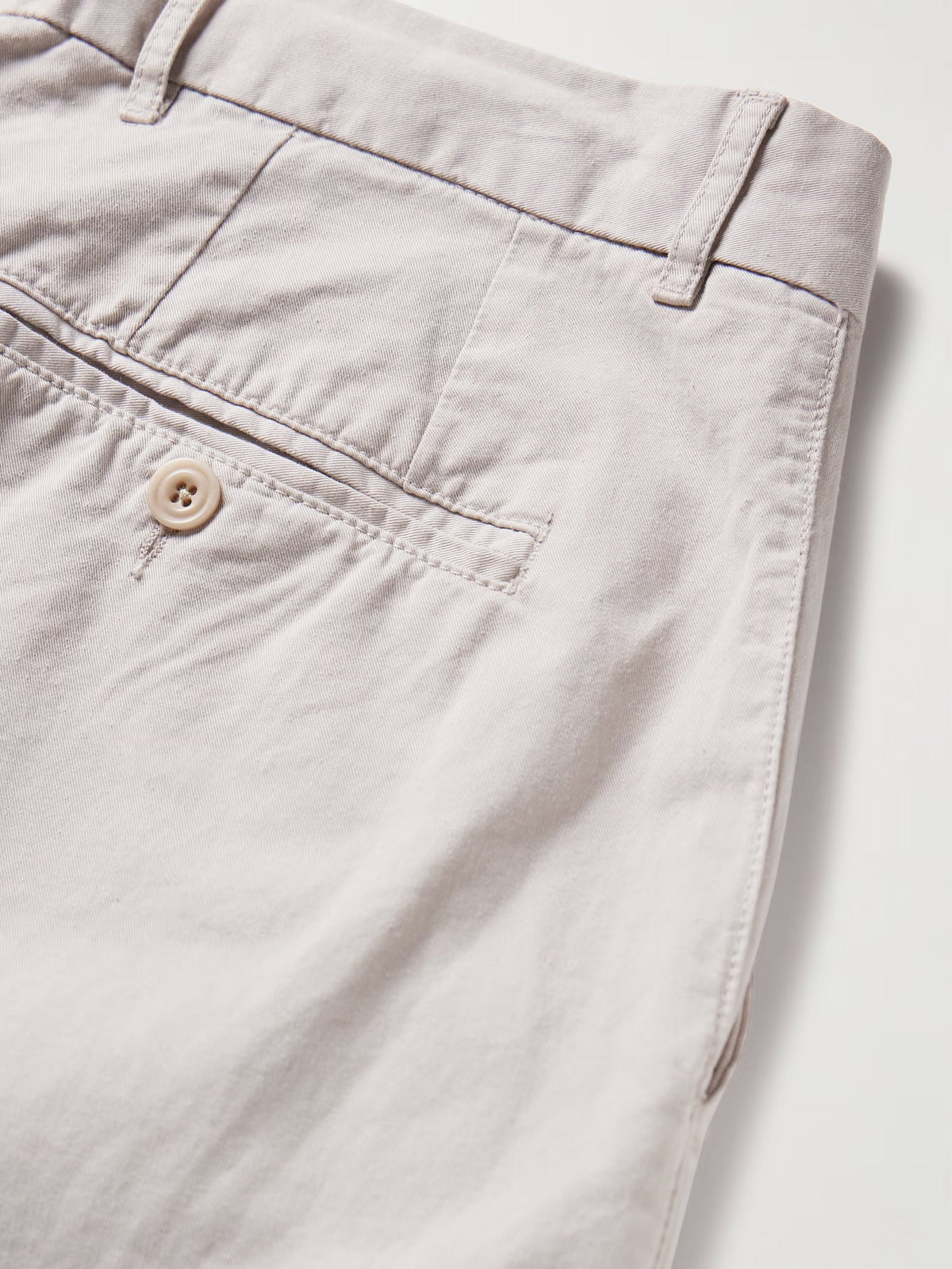 A person wearing HARTFORD - TAYLOR PANTS IN STONE, a white long-sleeve shirt, and black loafers stands on a wooden floor against a neutral wall.