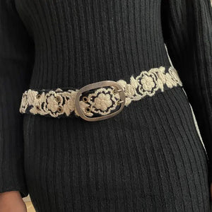 The JENNY KRAUSS Two Toned Belt in Black and Cream features intricate cream floral embroidery and a silver buckle, handmade in Peru. Shown coiled on a light background.