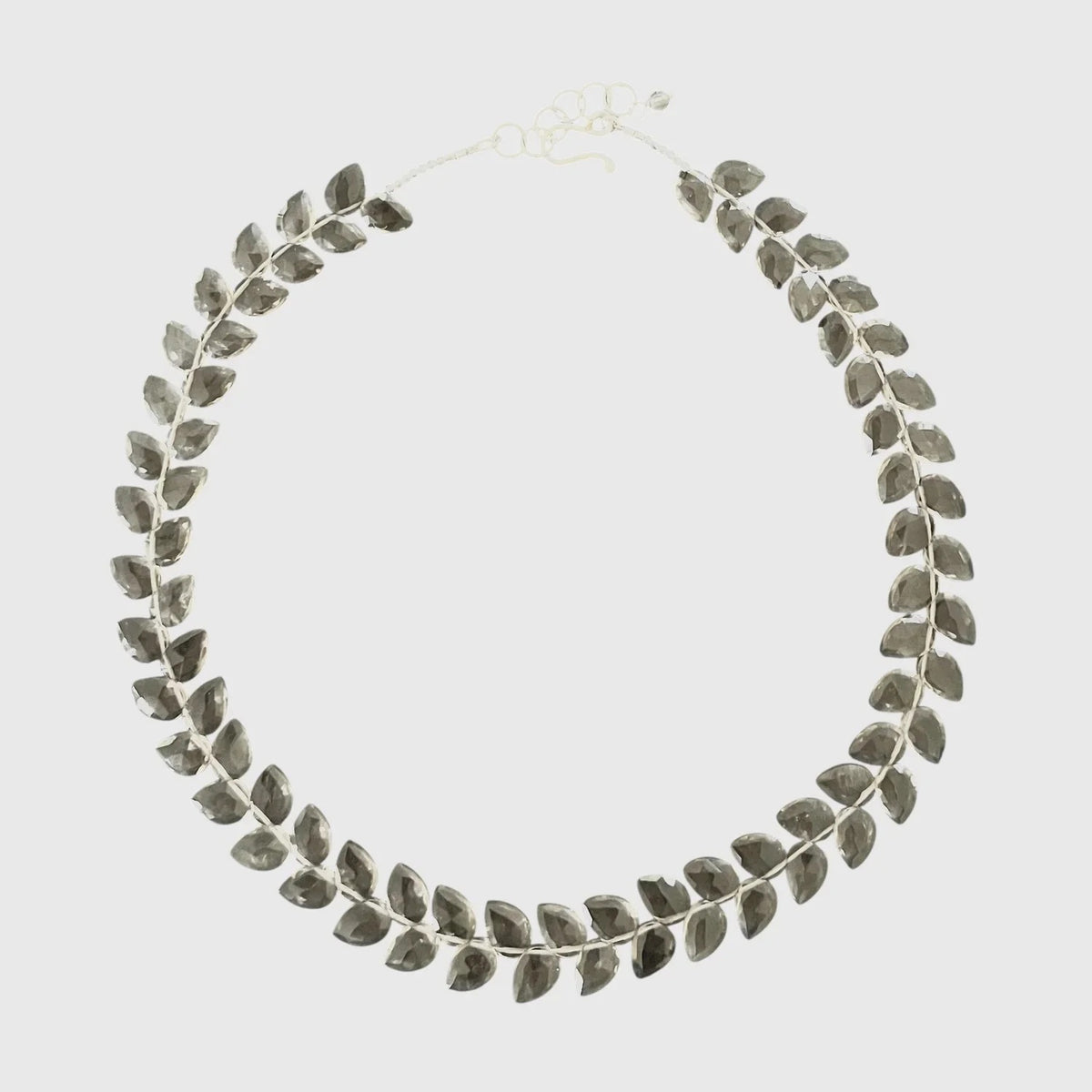 Shown from the shoulders up with their face partially out of frame, a person wears a textured, light beige fuzzy sweater and the ANN LIGHTFOOT Faceted Flat Herringbone Cut Smokey Quartz Necklace.