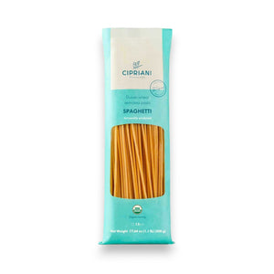 A white oval dish of Atalanta Corporation’s CIPRIANI – ORGANIC SPAGHETTI—made from premium organic durum wheat semolina—is topped with vibrant red tomato sauce and a fresh basil leaf, set atop a white tablecloth and surrounded by plates, cutlery, napkins, and glasses of water.
