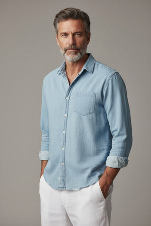 FRANK & EILEEN’s LUKE Men’s Button Up Shirt in Famous Denim Classic Denim Tattered Wash is showcased against a white background. Crafted from soft, premium denim, this light blue shirt features a single chest pocket, rolled-up sleeves, and a relaxed fit with a slightly wrinkled finish. The design is completed with an interior collar label.
