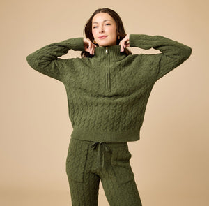 A woman wearing a marshmallow-soft, cream-colored SOFTIES - CABLE KNIT MARSHMALLOW ½ ZIP WITH TAPERED PANT SET, featuring a half-zip pullover and matching pants with a drawstring waist.