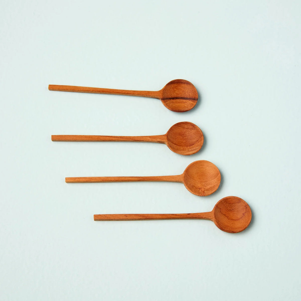 Four BE HOME - TEAK THIN SPOONs by BE HOME, INC., handcrafted from sustainably sourced wood, are arranged in a straight vertical line on a light, solid background.
