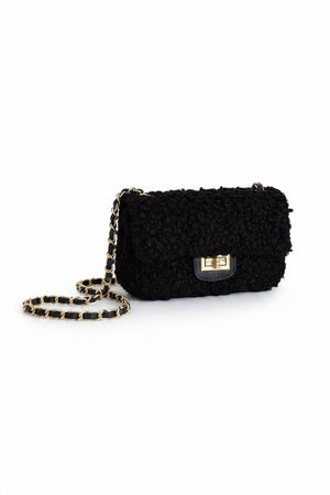 Introducing the VICARIO CINQUE - Brescia Handbag in Black by VICARIO CINQUE, featuring a bouclé exterior that evokes the look of curly wool. This elegant handbag is distinguished by its silver chain strap and rectangular silver clasp on the flap—an ideal accessory to infuse any outfit with a touch of Italian style.