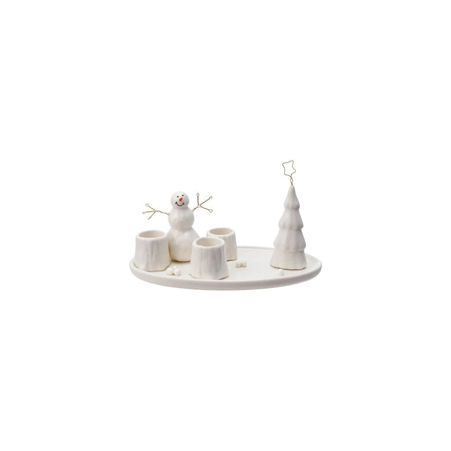 The STONEWARE TAPER HOLDER WITH SNOWMAN AND TREE by CREATIVE COOP features a snowy winter scene with a snowman, tree stump candle holders, and a Christmas tree on a round tray, perfect for festive holiday decor.