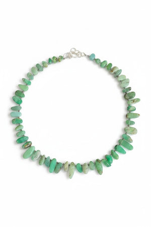 The ANN LIGHTFOOT Ras du Cou Necklace of Chrysoprase Pebbles features irregularly shaped green chrysoprase stones and a sterling silver clasp, elegantly displayed in a circular arrangement on a white background.