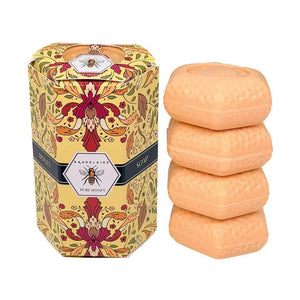 BAUDELAIRE Pure Honey Soap 1.4 oz Quartet, featuring a hexagonal honeycomb pattern and a bee emblem, is displayed with its coordinating floral packaging on a white surface alongside a honey dipper, soap bar, and natural bath sponge. Both the triple-milled BAUDELAIRE soap and box are adorned with the bee motif.