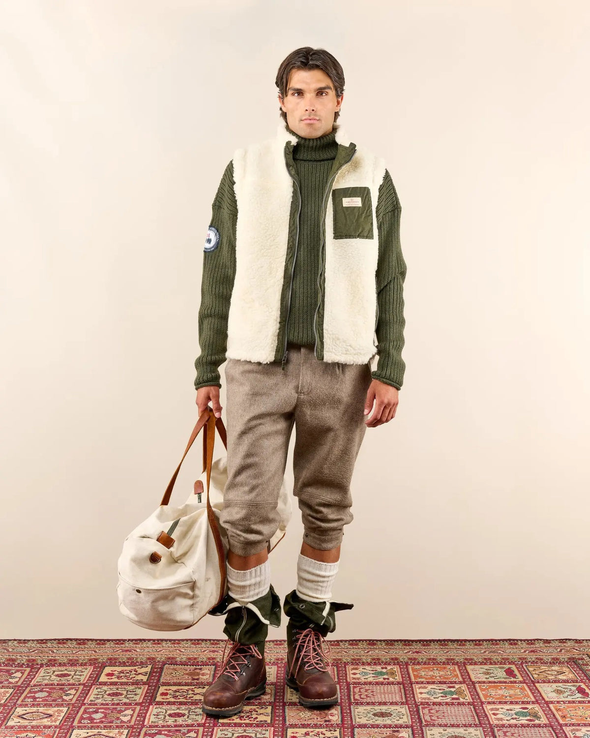 A man in the AMUNDSEN SPORTS - HARVESTER REVERSO WAXED COTTON VEST and sunglasses stands in shallow water with a fishing rod and net, surrounded by autumn trees.