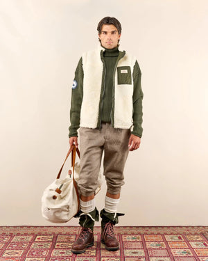A man in the AMUNDSEN SPORTS - HARVESTER REVERSO WAXED COTTON VEST and sunglasses stands in shallow water with a fishing rod and net, surrounded by autumn trees.