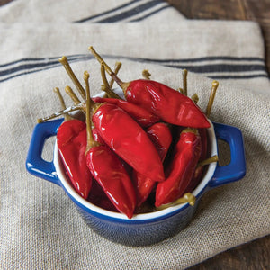 A glass jar of DIVINA - CALABRIAN PEPPERS by DIVINA, featuring a black lid, a red label, and sliced red peppers visible inside. The label highlights “Calabrian Peppers” and “Italy,” emphasizing these authentic Italian spicy peppers known for their bold flavor.