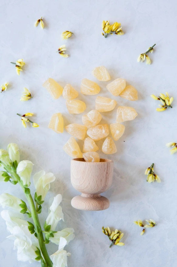The image displays a white packet of BUTTERFIELDS - GINGER BUDS hard candy. The front features an illustration of a ginger plant with red flowers and green leaves. The text reads &quot;Ginger Buds&quot; and &quot;Gluten Free,&quot; highlighting its natural ginger flavor, with the net weight shown as 2.5 oz (60 grams).