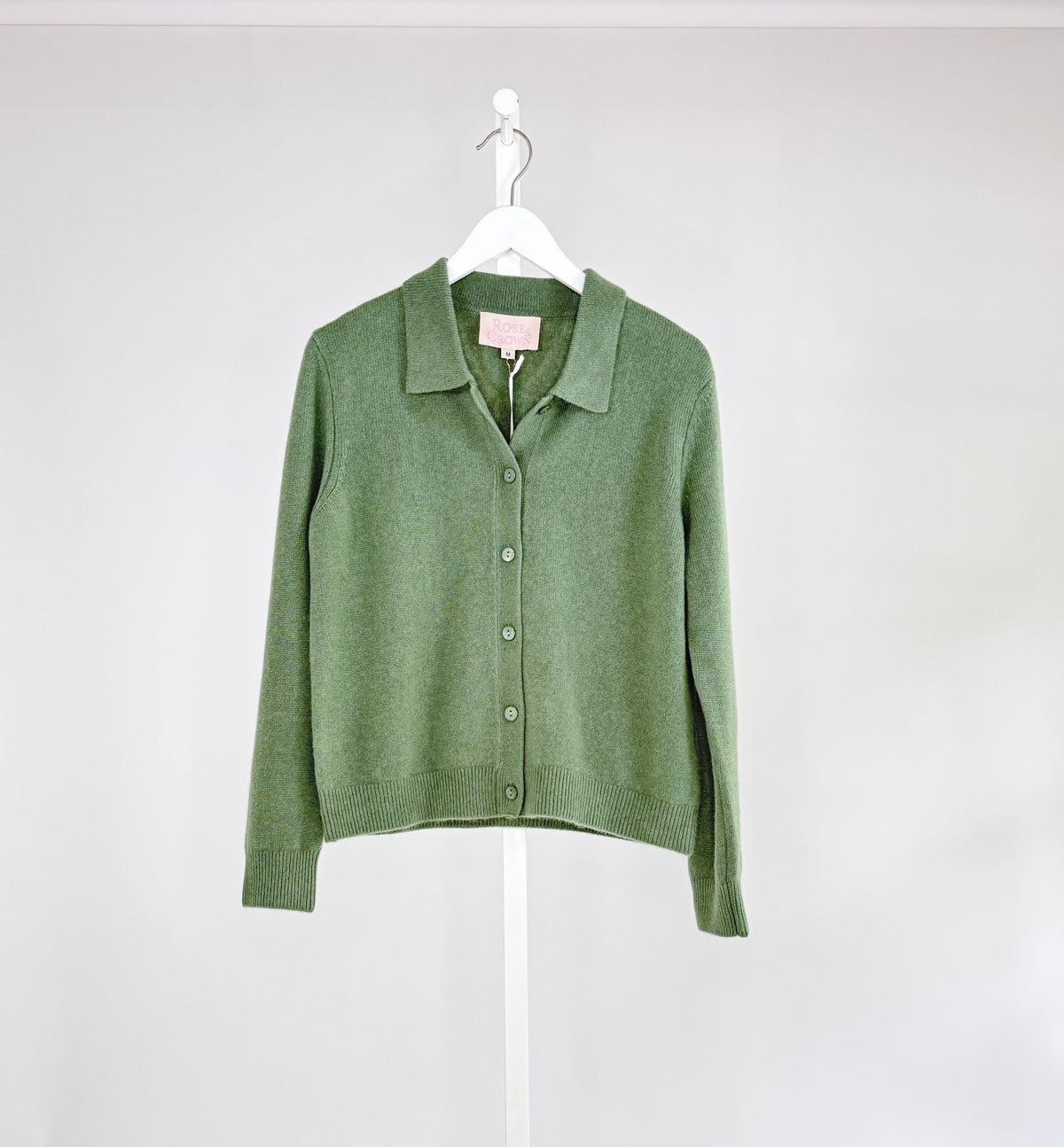 The ROSE &amp; CROWN - CASHMERE CARDIGAN, a luxury long-sleeve button-up in custom-dyed magenta, hangs on a white hanger against a light gray background.