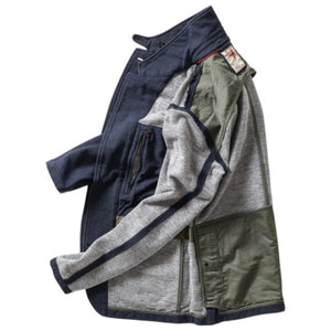 A person wearing the RELWEN - PIQUE TRAP BLAZER IN NAVY HEATHER over a checked shirt and green cargo pants stands with hands in pockets against a plain background, showcasing the blazer’s relaxed fit.