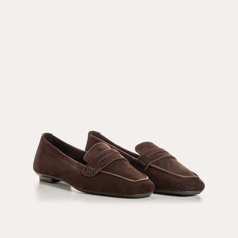 A person stands on a light floor wearing rolled-up blue jeans and REQINS HEMA suede loafers in Marron, showcasing the artisanal craftsmanship of REQINS.