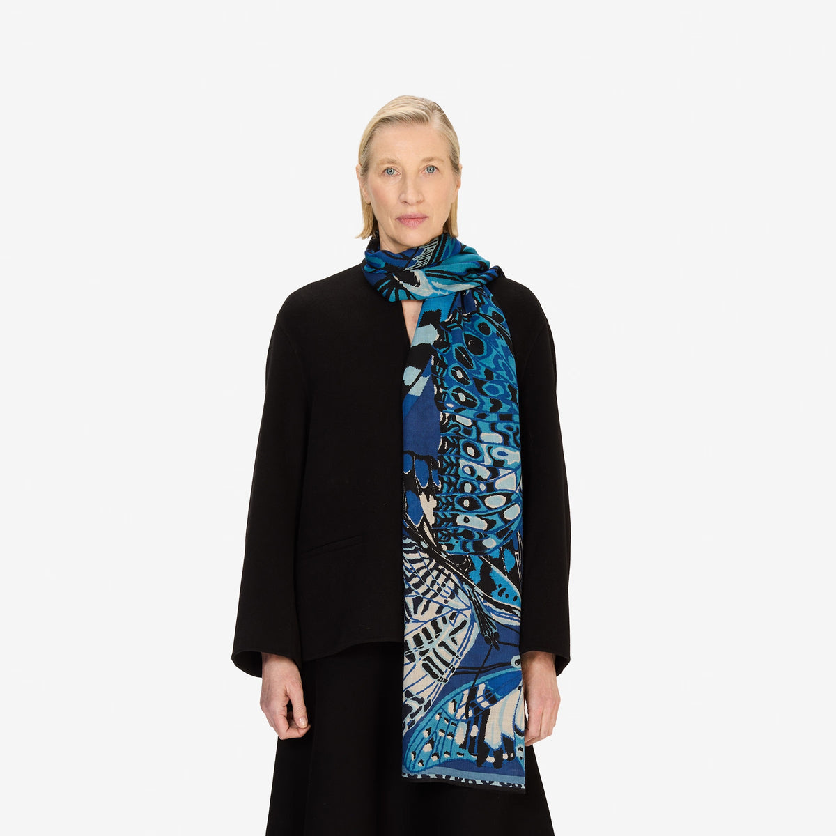 A person wearing a beige knit sweater and an INOUI EDITIONS - PAPILLON (BUTTERFLIES) Wool Scarf in Navy by INOUI, made in India, wrapped around their neck, shown from the chin to the chest.