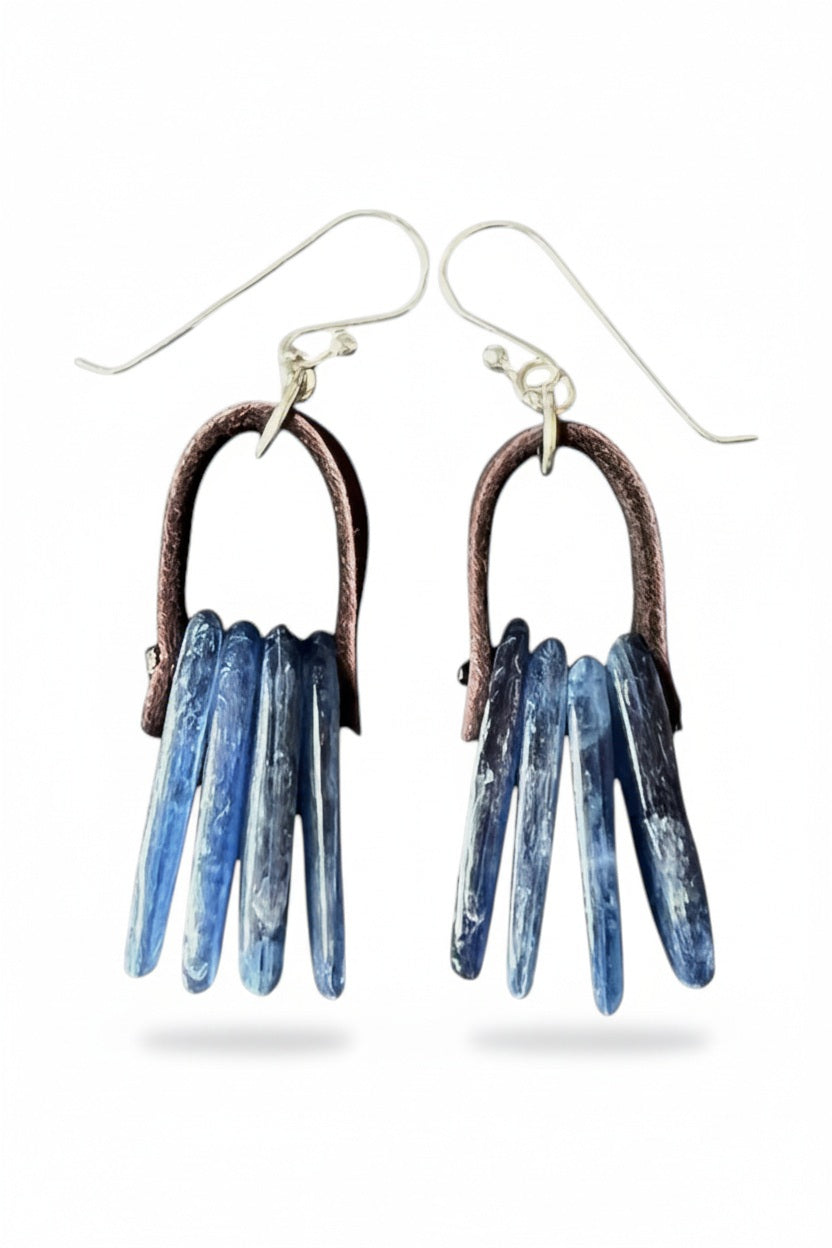Add a touch of modern elegance to your look with the ANN LIGHTFOOT - KYANITE SLABS WITH DARK BROWN LEATHER EARRINGS. These striking earrings by ANN LIGHTFOOT feature captivating blue kyanite slabs gracefully suspended from dark brown leather loops and finished with sterling silver earwires. Shown against a white background, their unique design highlights the natural beauty and expert craftsmanship of this accessory.