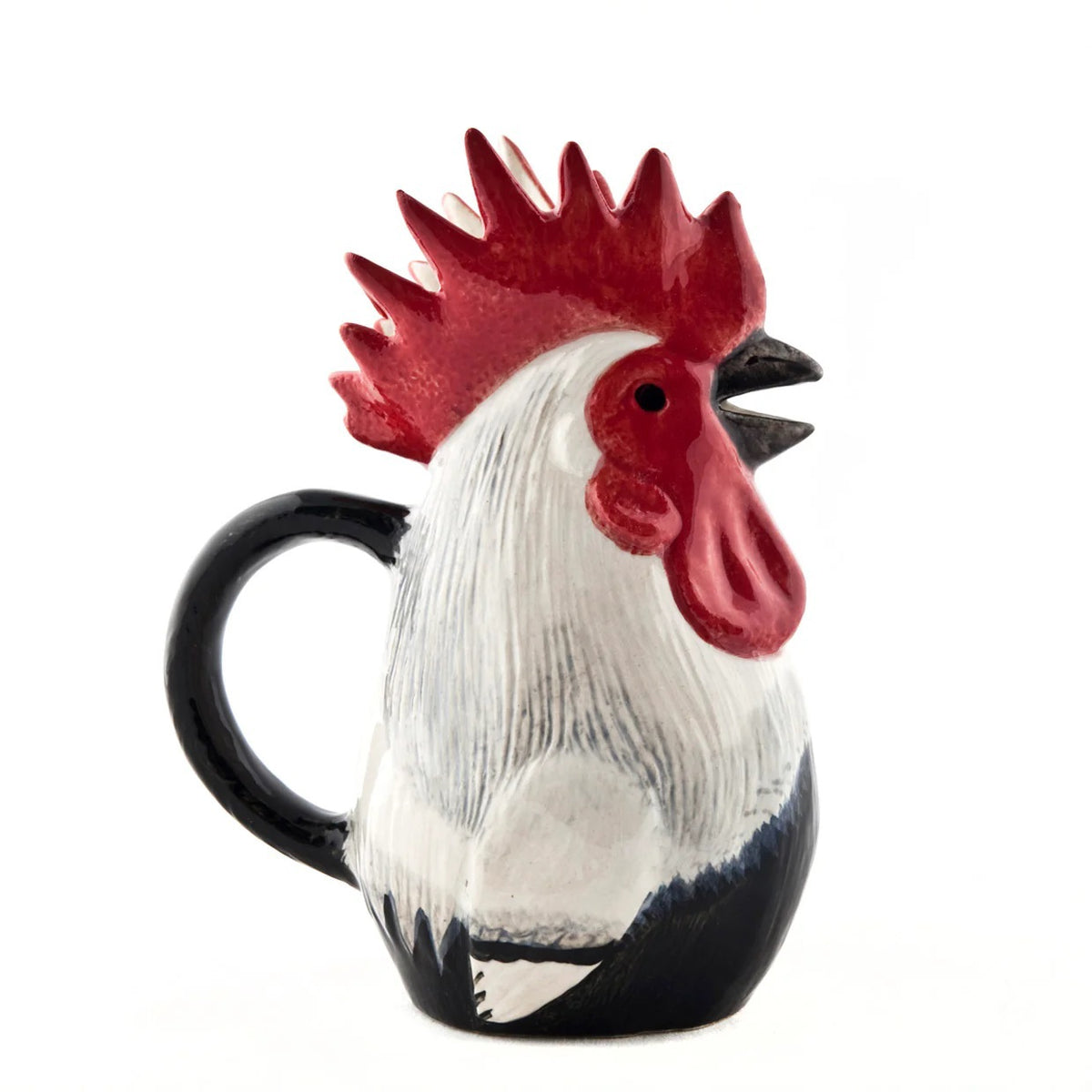 The QUAIL CERAMICS - DORKING ROOSTER JUG by QUAIL DESIGNS, a hand-painted stoneware jug with a red comb and black handle, sits on the table beside a green glass and patterned plates—a charming British tea accessory.