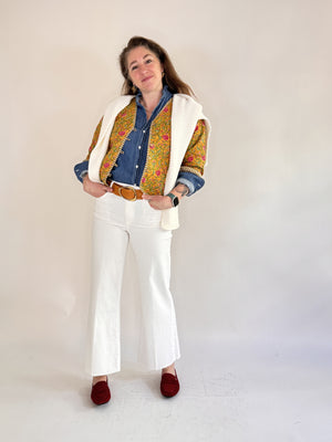 A woman with visible forearm tattoos smiles slightly against a plain background, wearing the FARYLINA ZOIE Reversible Quilted Jacket over a denim shirt, white pants, and a tan belt.