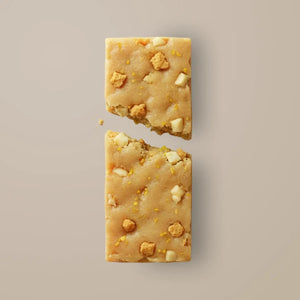 A STARS+HONEY - ICED LEMON COOKIE collagen protein bar in a vibrant yellow wrapper, featuring cookies adorned with white icing and gold sprinkles—some whole, some crumbling—bursting outward against a beige backdrop, capturing a healthy snack from STARS+HONEY packed with delicious flavor.