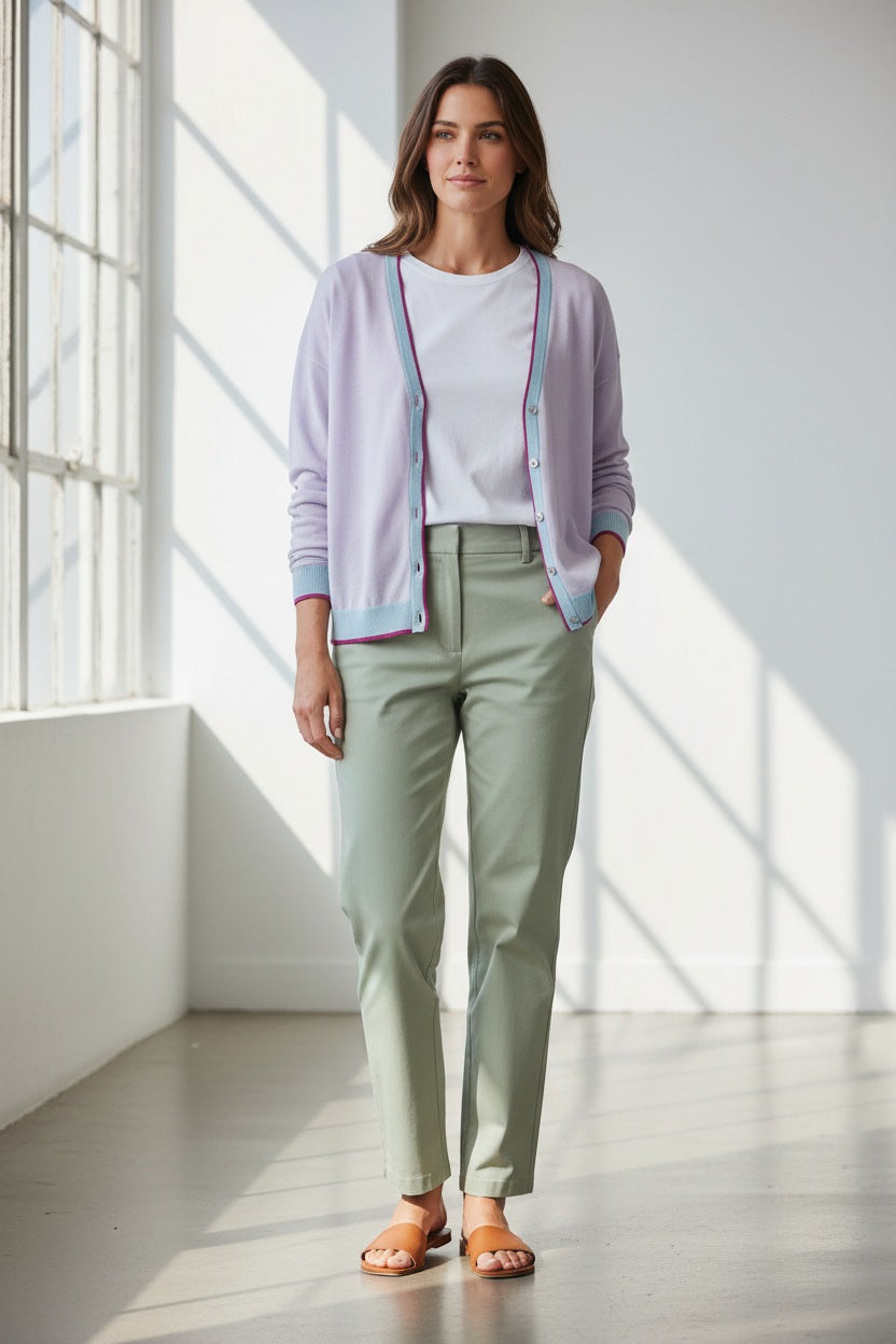 A woman wears the IN BED WITH YOU - BATWING SLEEVE CARDIGAN by IN BED WITH YOU/CLAUDIOLAI SRL, an orange V-neck with red and white trim, buttoned down the front, styled with multicolored patterned pants against a plain white background.