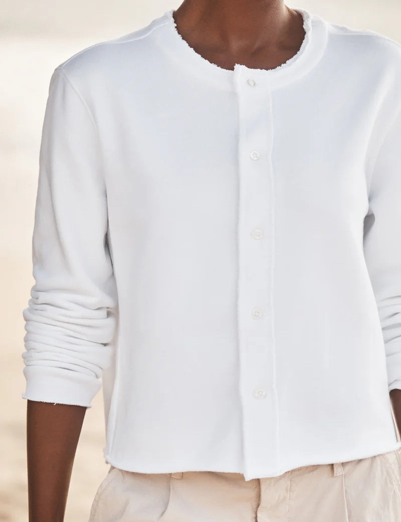 A woman stands on the beach in the FRANK &amp; EILEEN JACKIE Sweatshirt Cardigan in white, gazing sideways with the ocean and sky behind her.