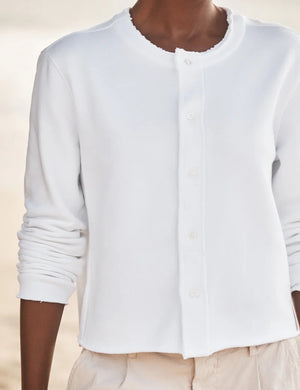 A woman stands on the beach in the FRANK & EILEEN JACKIE Sweatshirt Cardigan in white, gazing sideways with the ocean and sky behind her.