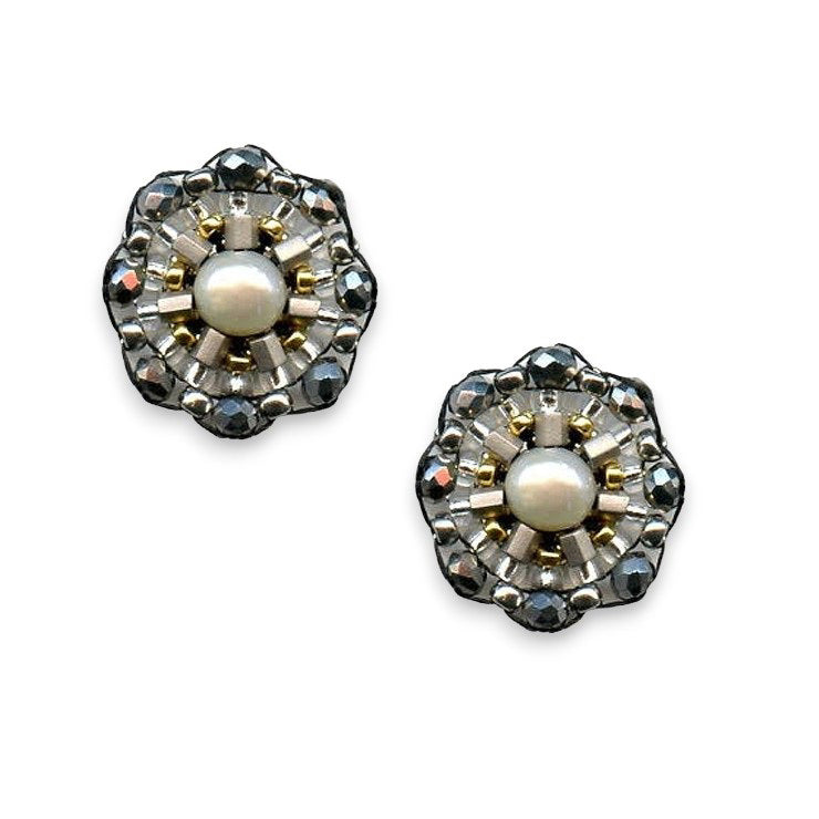 The MIGUEL ASES - PYRITE SILVER RONDELLE STUD EARRINGS from MIGUEL ASES, INC. feature a central pearl encircled by 14K gold-filled concentric layers of metallic beadwork and small black gems, creating a flower-like design with intricate handcrafted detailing.