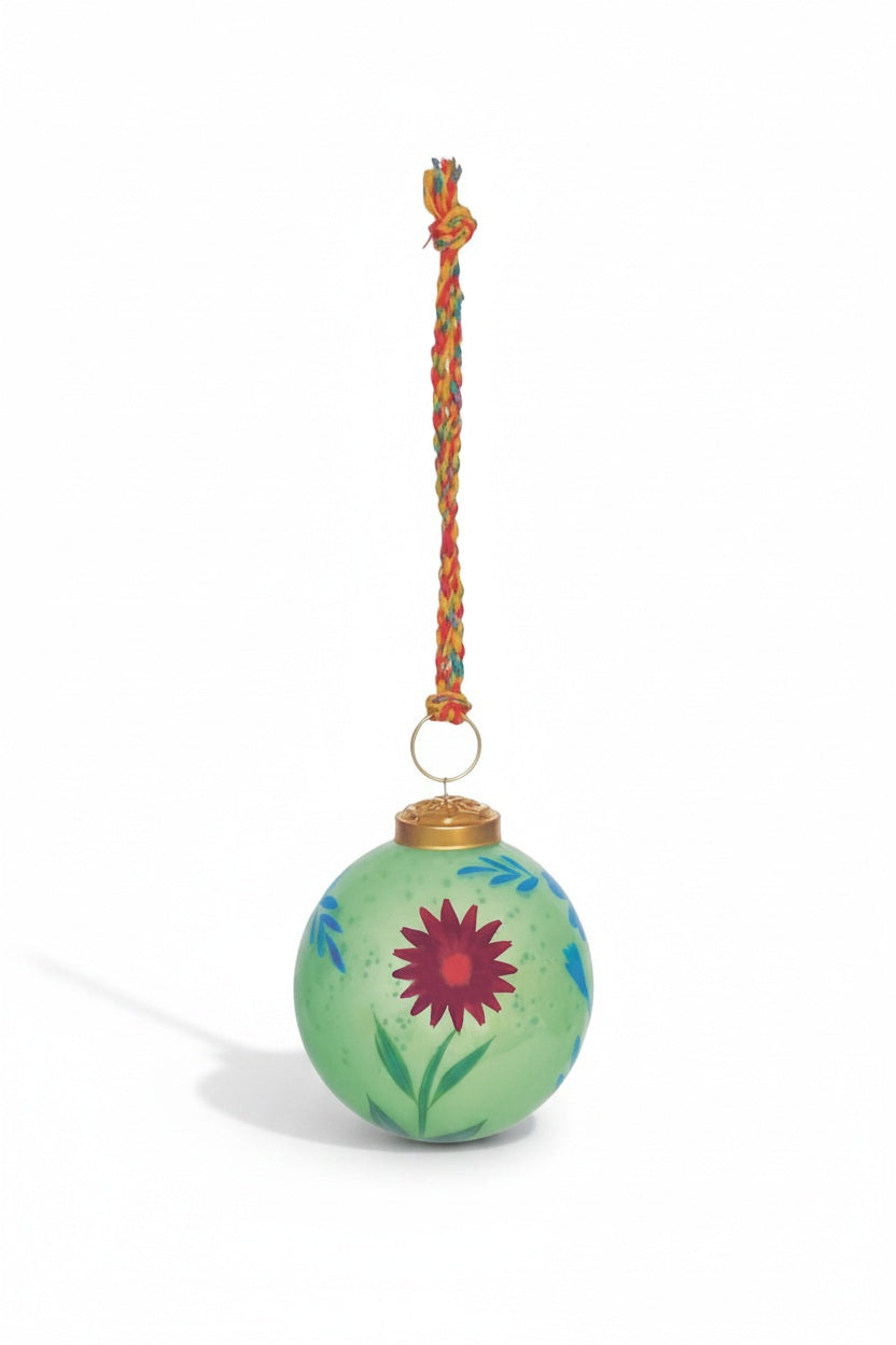 A round green GLASS BALL ORNAMENT WITH FLOWERS decorated with a hand-painted red flower and a multicolored braided fabric hanger.