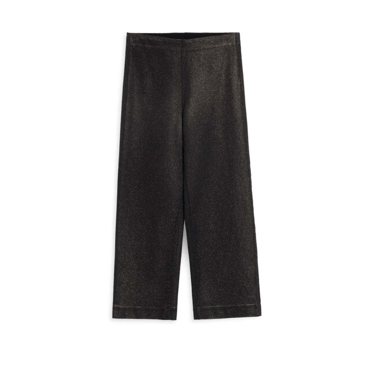 A woman stands in a doorway wearing a light blue shirt and FRANK &amp; EILEEN’s WESTPORT ILLUSION Wide Leg Pull-On Pant in Black Gold Glitter. A cozy living room with a sofa, lamp, and plants is visible in the background.