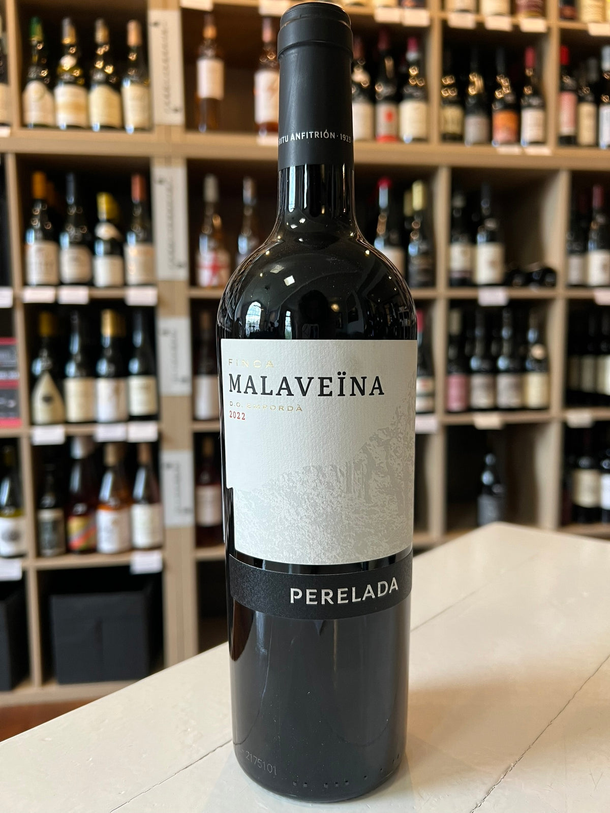 A PERELADA 'FINCA MALAVEÏNA' MERLOT BLEND 2019 wine bottle from Empordà, Spain, features a black label with silver text and a horse-drawn carriage logo. The black cap elegantly displays "Malaveïna" in silver lettering. Enjoy its smooth tannins. Brand: WINE: JOHNSON BROS./MUTUAL/EPIPHANY.