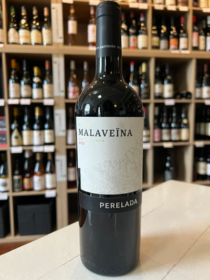 A PERELADA 'FINCA MALAVEÏNA' MERLOT BLEND 2019 wine bottle from Empordà, Spain, features a black label with silver text and a horse-drawn carriage logo. The black cap elegantly displays "Malaveïna" in silver lettering. Enjoy its smooth tannins. Brand: WINE: JOHNSON BROS./MUTUAL/EPIPHANY.