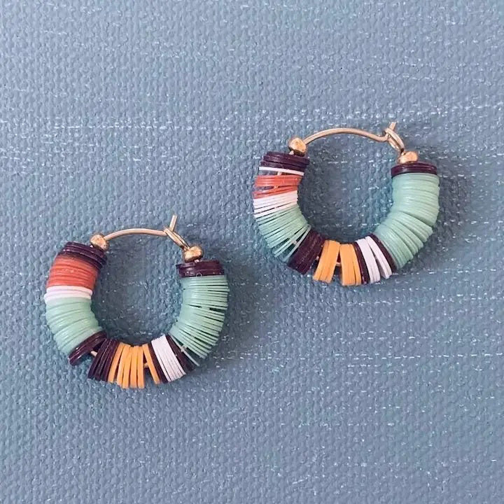 The ALICE RISE ALISE RISE - POOLSIDE HOOP EARRINGS feature stacked, colorful recycled African vinyl beads in teal, black, white, yellow, and rust—a unique handmade statement for vibrant style.