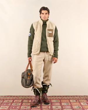 The AMUNDSEN SPORTS - HEROES FLEECE VEST NATURAL is a beige sherpa wool fleece vest with a zip front, two hand-warmer pockets, brown waxed cotton chest pocket with label, high collar, and rounded dropped back hem.