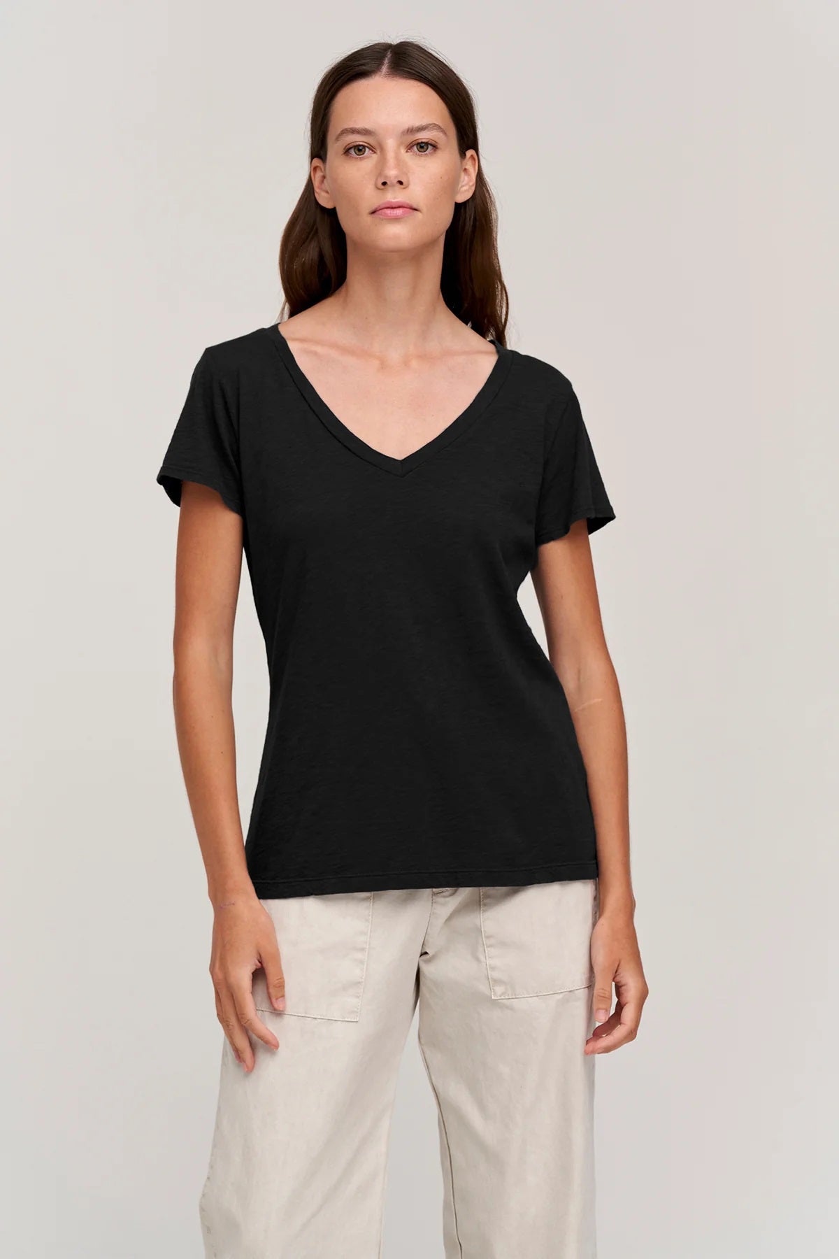 A person with shoulder-length brown hair is standing with their back to the camera. They are wearing a VELVET BY GRAHAM &amp; SPENCER&#39;s LILITH V NECK SLUB COTTON TEE in blue and light blue jeans. The background is a plain, light-colored wall.