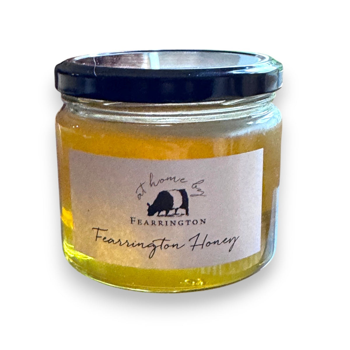 The Fearrington Signature Collection's hexagonal glass jar elegantly holds their Wildflower Honey, known for its raw quality. The label states: "Raw, Unfiltered. Handmade with care in our kitchens. May contain allergens. 282 grams, 10 oz." Inside is the finest golden honey from Fearrington House.