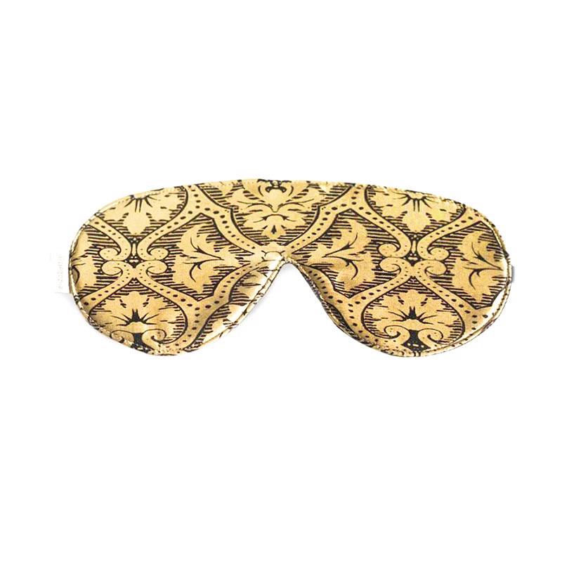The GOLD DAMASK SLEEP MASK by E WIGHTMAN &amp; CO is a gold and black patterned adjustable silk eye mask featuring an intricate design with symmetrical, ornate motifs reminiscent of classic, vintage styles. It is shaped to cover the eyes comfortably and provides a stylish way to block out light, helping you sleep soundly.