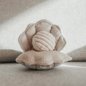 The LAMBWOLF COLLECTIVE - OYSTER POP DOG TOY by LAMBWOLF COLLECTIVE is a soft, plush toy representing a light beige shell with a round, textured pearl inside. Crafted from a corduroy-like material, the shell and pearl showcase multiple textures, giving them a cozy and inviting appearance. This Sea World Edition toy is displayed against a neutral fabric background.