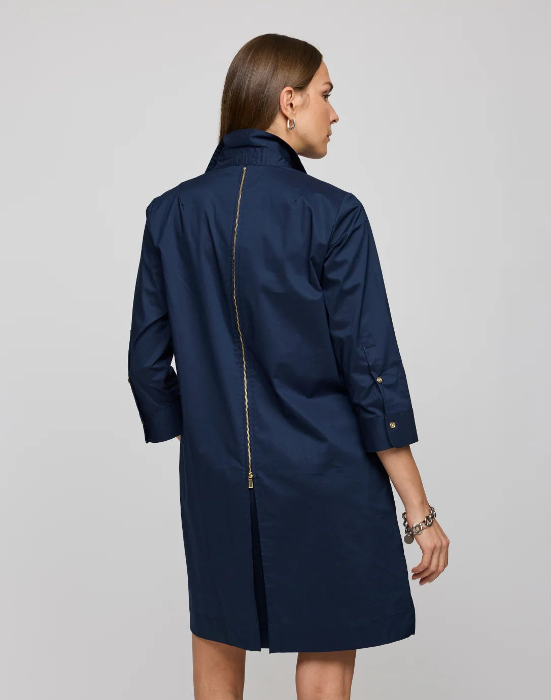 A woman with straight brown hair models the HINSON WU - ALESSA 3/4 SLEEVE DRESS IN STRETCH POLISHED COTTON NAVY, featuring a boxy fit, knee-length cut, three-quarter sleeves, and a visible back gold zipper against a plain background.