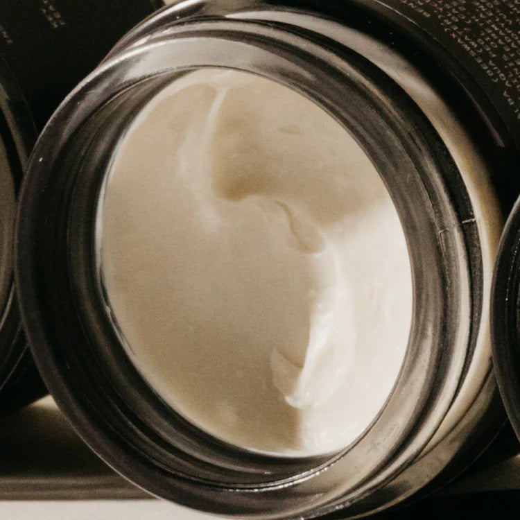 A close-up shot of an open jar filled with PRESTON - CREAM POMADE UNSCENTED. The smooth, frizz-free texture of the pomade is visible within the dark-colored container. The jar is placed on its side against a neutral background.